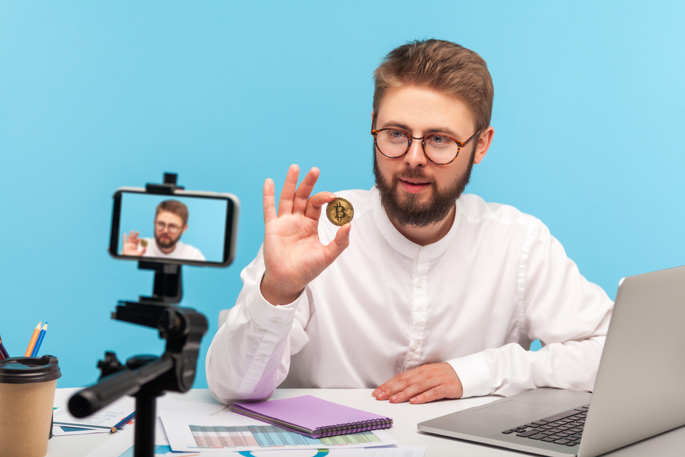 man-holding-a-bitcoin-up-to-a-camera